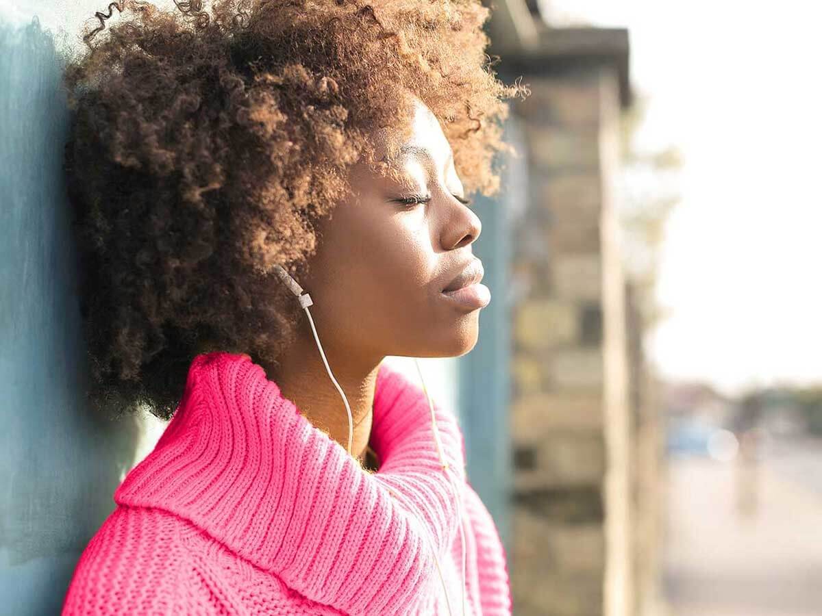 Woman listening to music whilst standing against a wall