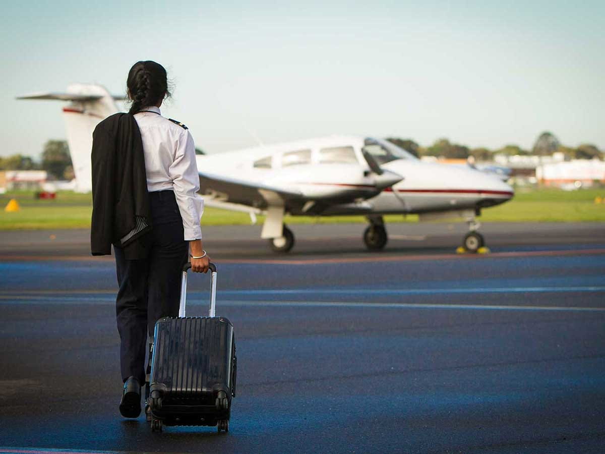 A pilot carrying a suitcase is walking towards a plane