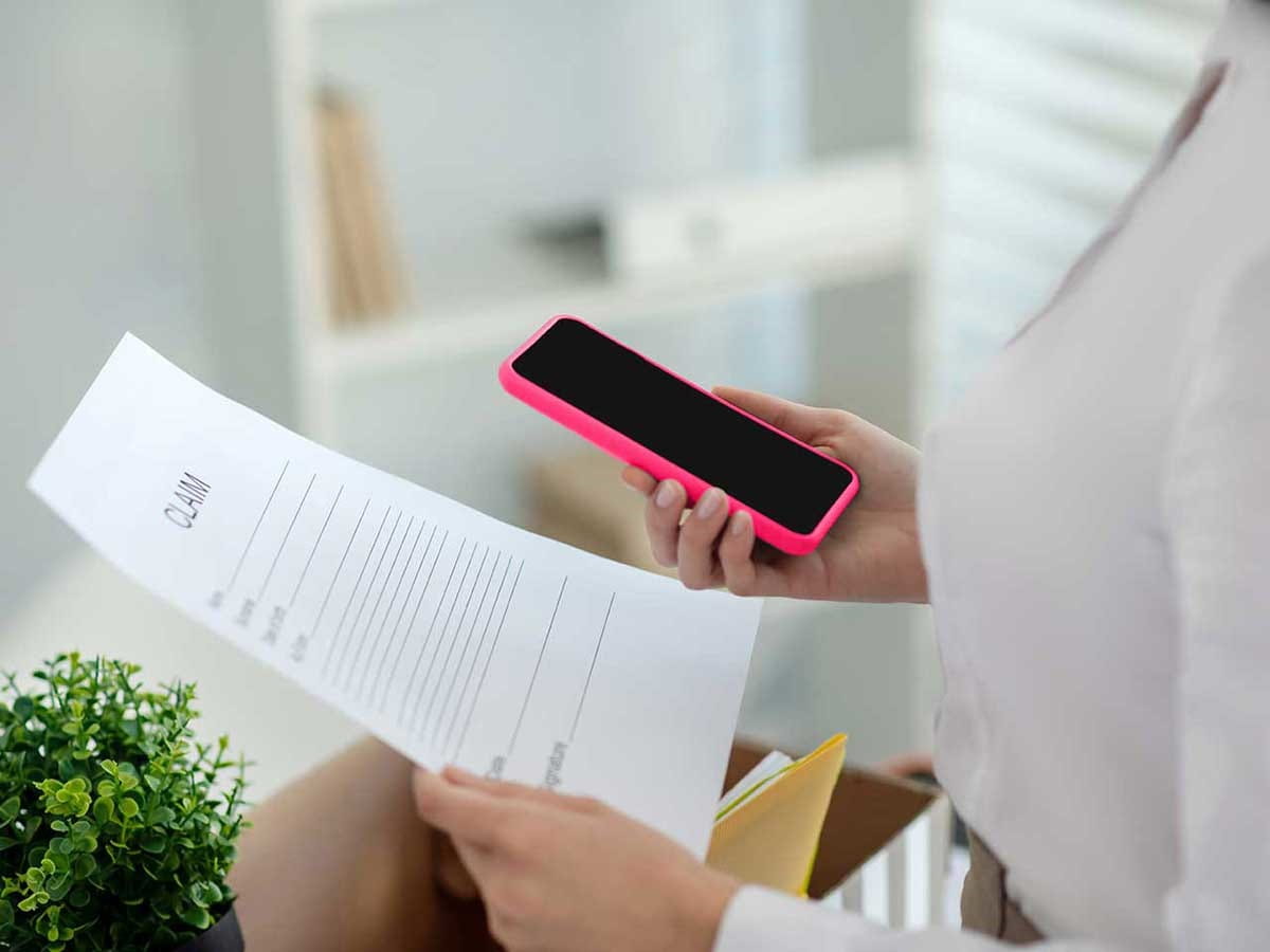 Woman looking at claim form whilst holding a phone