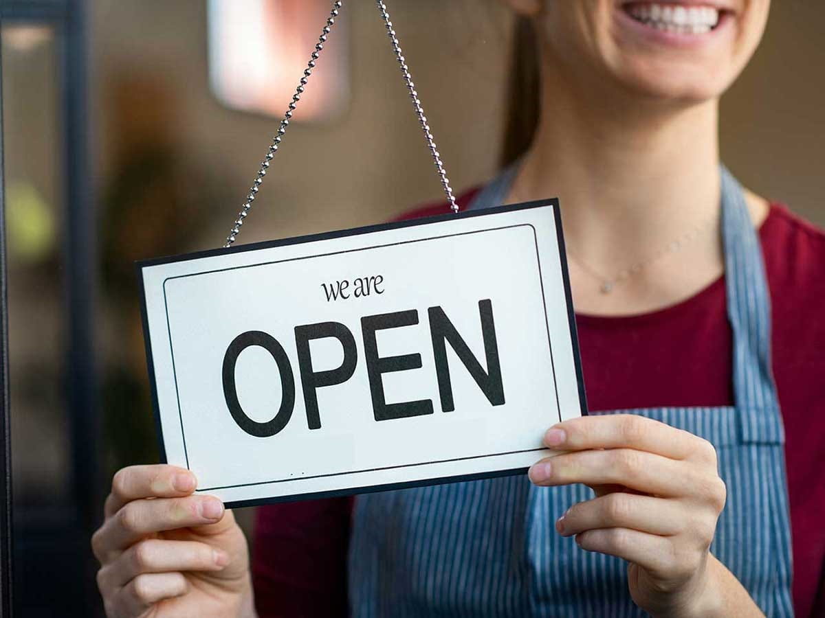 A woman holding up the open sign in her shop window