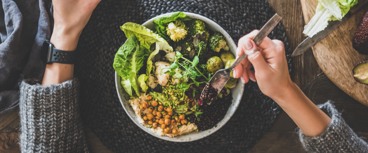Healthy dinner, lunch setting. Flat-lay of vegan championship game or Buddha bowl with hummus, vegetable, salad, beans, couscous and avocado, green smoothie and woman's hands over wooden table, top view