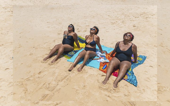 Three Black women relaxing and laughing on the beach
