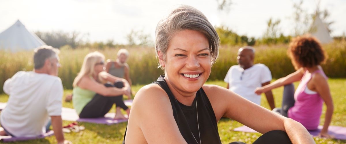 smiling woman outside on a yoga mat