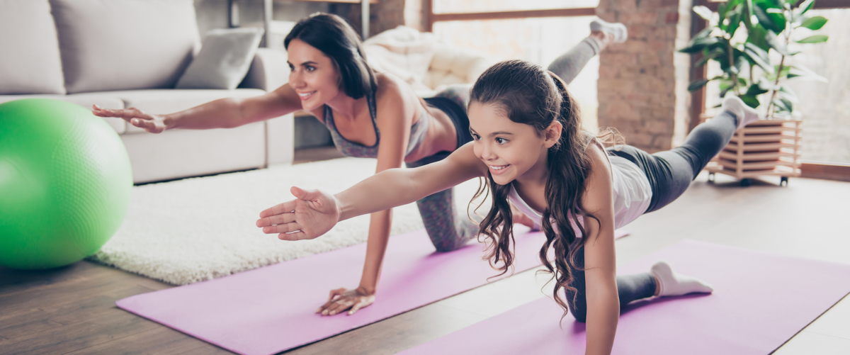 Vitality concept. Watch repeat the moves, poses from the helpful video! Cute sweet cheerful joyful with long hair schoolgirl and slim sportive mom are doing stretching exercises in room om purple mats