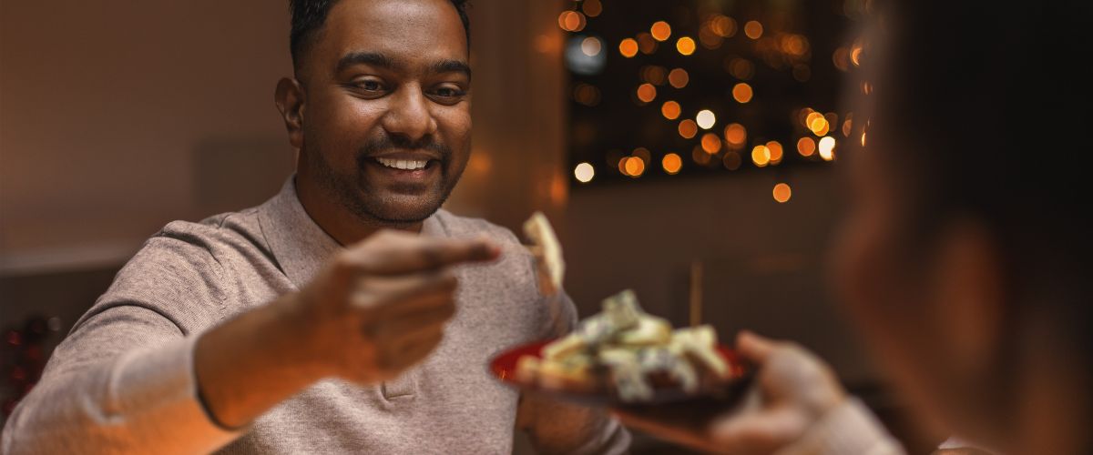 man taking a bite to eat from a plate with twinkling lights in the background
