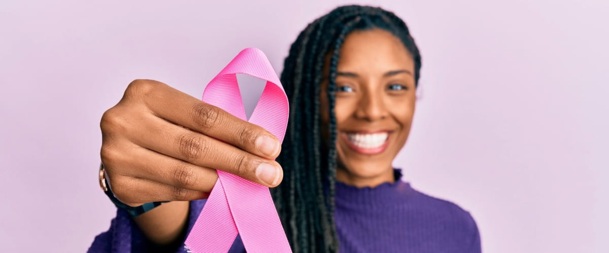 Person holding a pink breast cancer awareness ribbon towards the camera.