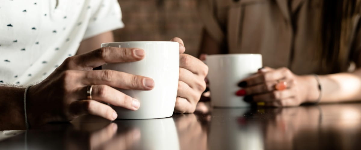 two-people-with-hands-around-coffee-mugs