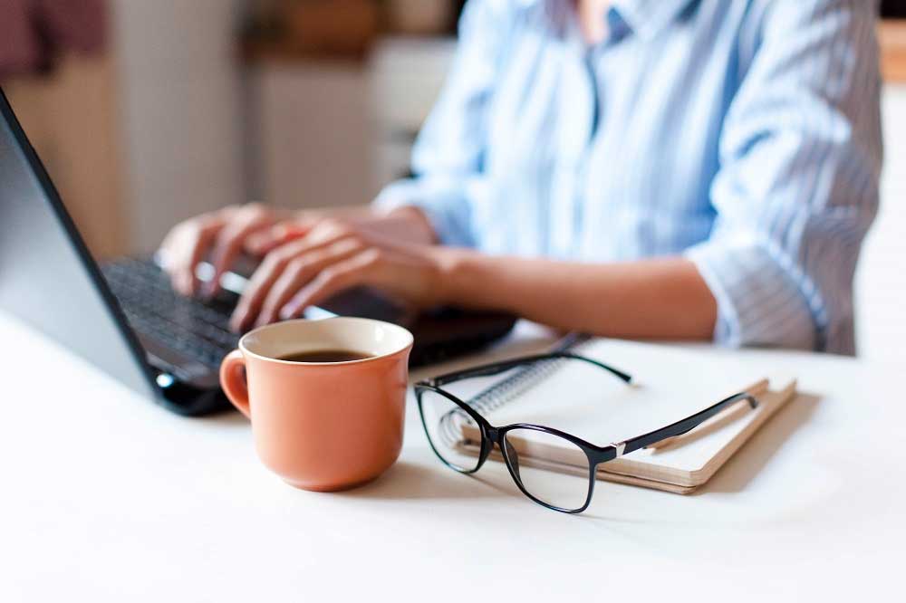 Woman at laptop with coffee and notebook on table