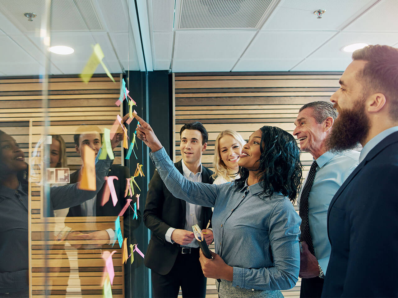 Colleagues putting sticky notes on glass wall